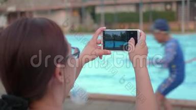 女士通过智能手机拍摄度假游泳池。