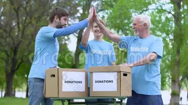 快乐的志愿者奉献高五，捐赠箱在桌上，慈善活动