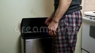 一个男人把垃圾/回收到家里厨房里的金属回收/垃圾容器里。