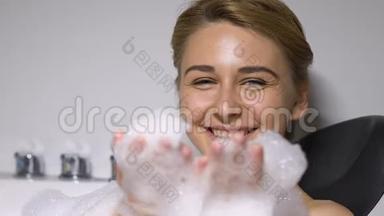嬉戏的年轻女士在浴缸里吹<strong>泡沫塑料</strong>，享受乐趣、休闲和放松