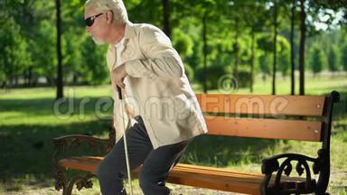 盲人带着拐杖从长椅上站起来，在夏季公园散步，放松身心