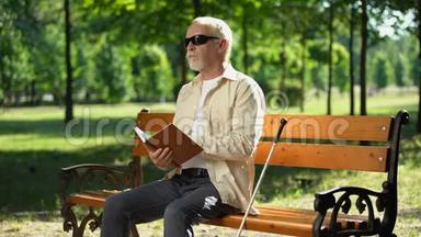 令人沮丧的盲人退休男子无聊的盲文书，感到沮丧的独自在公园