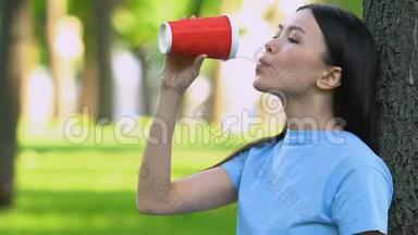 女孩在塑料杯里喝鸡尾酒，在草地上扔垃圾，乱扔垃圾