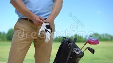 男高尔夫球手在比赛前戴白手套，包在附近有运动器材