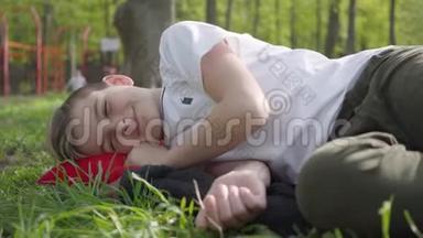男孩躺在操场附近的草地上，在温暖的春日周末<strong>放学</strong>后心烦意乱或疲倦