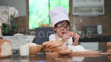 可爱的亚洲小男孩带着眼镜、厨师帽和围裙，带着鸡蛋，第一次体验到家中的烘焙面包店