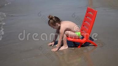 在沙滩上坐在海边的椅子上和海浪玩耍的小女孩