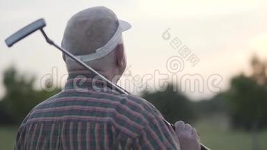 在高尔夫球场打高尔夫球的成熟男人的后景。 一个年长的人肩上扛着球杆向外看。 老了