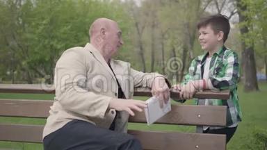 那个秃顶的成熟男人拿着一本书坐在公园的长凳上，和他的孙子说话。 然<strong>后人</strong>们握手