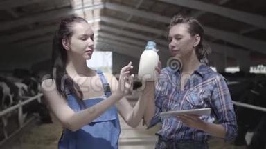 肖像两名专业可爱的女农民工人在奶<strong>牛</strong>场检查<strong>牛奶瓶</strong>的质量。 一个