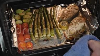 厨师把鱼从烤箱里弄出来。 烤鲑鱼和蔬菜在电烤箱里。 女人在家做美味的晚餐。 准备好的鱼和