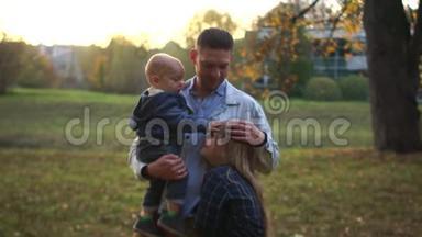 年轻迷人的父亲带着两个孩子在公园里散步。 一个男人抱着一个小儿子拥抱女儿