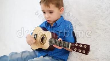 一个快乐的孩子坐在白色的沙发上弹着孩子们`吉他和唱歌