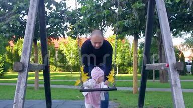 爸爸和他可爱的小女儿站在秋叶秋千附近，妈妈来了，带来了美丽的黄叶
