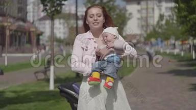 年轻漂亮的红发妈妈抱着一个可爱的小男孩在春天阳光明媚的日子里和他说话。 妈妈带着