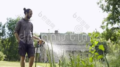 年轻英俊的嬉皮士用花园软管浇灌花园。