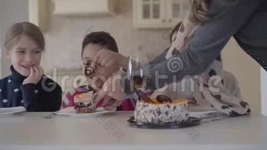 三个孩子在桌子上拿着小蛋糕和果汁眼镜。 女人的手切蛋糕，给男孩放一块`盘子