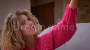 特写镜头漂亮的家庭主妇穿着粉红色毛衣，在智能<strong>手机</strong>上<strong>制作</strong>自拍照片，在家庭氛围中。