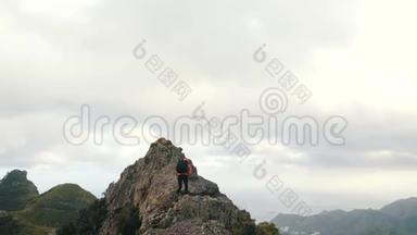背着背包的年轻女子爬上一座锋利的山脊，到达山顶。 在山顶上的女士