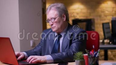 高级商人的肖像，穿着正式服装，在办公室同时使用笔记本电脑和智能手机。