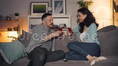 男人和女人说话，碰杯，喝着酒，坐在家里的沙发上