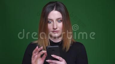 年轻的女商人带着栗色的头发，在绿色背景下<strong>困惑</strong>和<strong>困惑</strong>地看着手机。