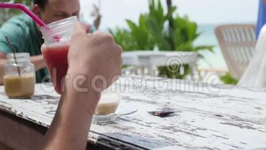 海滩上的夏日水果鸡尾酒。两个朋友在海滩上的咖啡馆喝鸡尾酒。鸡尾酒和椰子