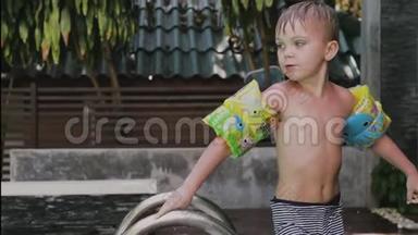 穿着袖子和帽子的小男孩在度假时跳进游泳池。 男孩在热带的游泳池里游泳。 儿童潜水