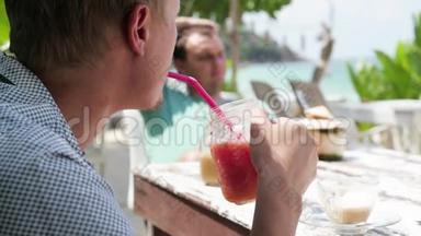 海滩上的夏日水果鸡尾酒。两个朋友在海滩上的咖啡馆喝鸡尾酒。鸡尾酒和椰子