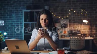 使用智能手机触摸屏幕的年轻女士在晚上加班