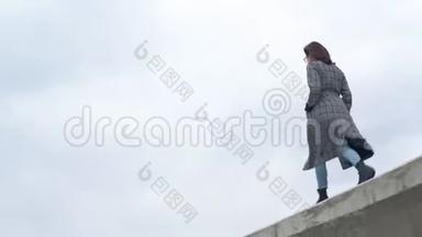 一位年轻女子走在水泥栅栏上。 穿外套的女孩