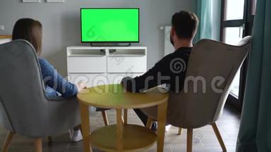 男人和女人坐在椅子上，用绿色的屏幕亲吻和看电视，用遥控器切换频道
