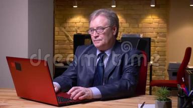 戴眼镜和穿着正式服装的老人在办公室里用笔记本电脑工作时生气和恼怒的肖像。