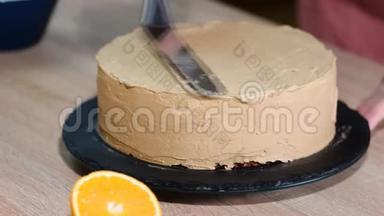 在巧克力海绵蛋糕上涂上奶油的特写。 家庭烘焙。 蛋糕在旋转的支架上装饰蛋糕。