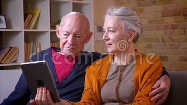 年长的白种人<strong>配偶</strong>观看平板电脑，并讨论它是积极和高兴的沙发在客厅。