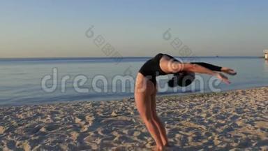 在海边或海边的沙滩上做瑜伽的女人。 穿黑色紧身衣的女孩练习和放松。 健康概念。 4k. 4k
