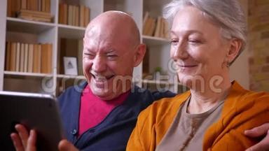 在舒适的家里，一对老白种人夫妇在平板电脑上和他们的朋友一起玩网络视频游戏。