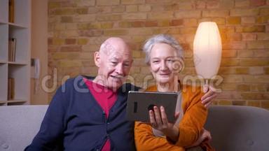 两位年长的白发白种人配偶在平板电脑上有一个视频卡，在舒适的<strong>家中</strong>既有趣又快乐。