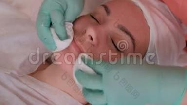 一个女孩闭着眼睛在美容院做一个恢复活力的手术。 手套里的美容师的手.. 专业的美容师