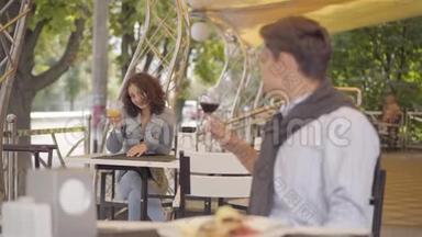 年轻人喝着红酒坐在前台，举起酒杯看着坐在前台的漂亮女人
