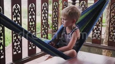 一个快乐的小男孩躺在吊床上玩耍。 夏天，小男孩躺在阳台上的吊床上。