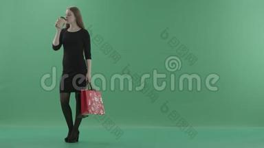 穿着黑色<strong>小裙子</strong>的漂亮女人正在喝咖啡或茶，拿着她的购物袋。 她站在左边