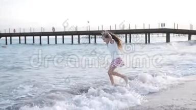 可爱的小女孩在海滩上日落时跳跃。 孩子喜欢在海边玩耍，在水上嬉戏