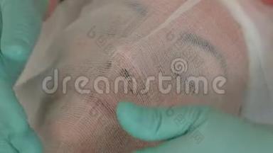戴着绿色手套的美容医生的手被纱布覆盖在女人`脸上。 一个漂亮的女孩正在做一个手术