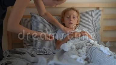 一个生病的小男孩躺在床上。 母亲用精油`男孩胸部涂抹药膏，测量他的体温。 宝贝