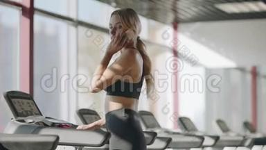 苗条的运动女人在健身馆里讲手机。 健身女孩步行跑步机
