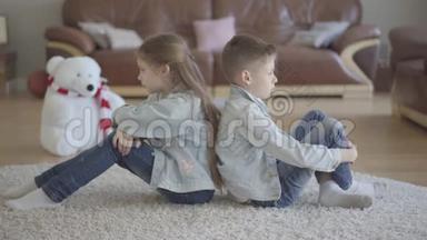 肖像双胞胎白种人男孩和女孩坐在客厅的地板上，背对着对方生气。 兄弟和兄弟