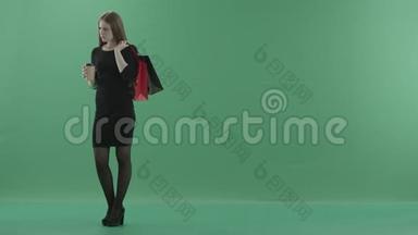 穿着黑色小裙子的漂亮女人正在喝咖啡或茶，拿着她的购物袋。 她站在左边