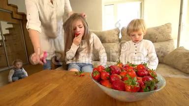 女孩吃草莓，母亲梳头发和兄弟。 红熟的浆果