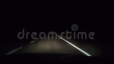 在夜间轨道上从出租车上看到。 大灯照亮了汽车前面的沥青。 迎面而来的车辆的大灯是黑色的